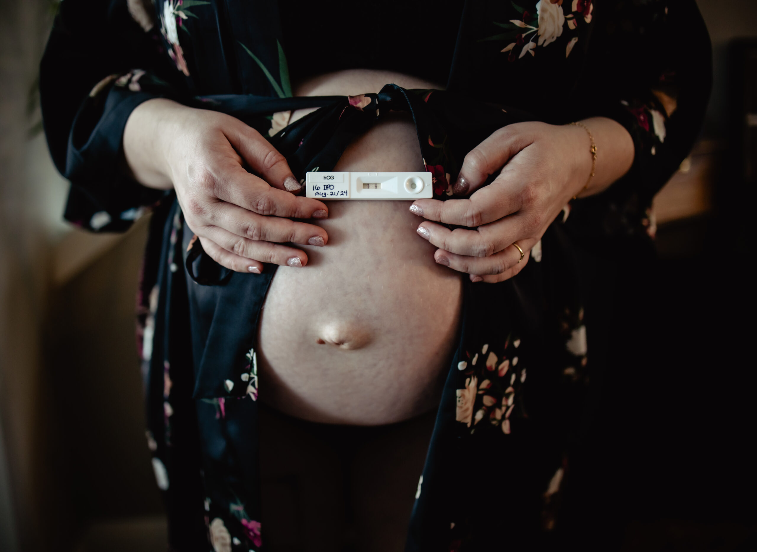 Pregnant belly with hands holding a pregnancy test — a sweet announcement detail in a creative maternity photo outfit.