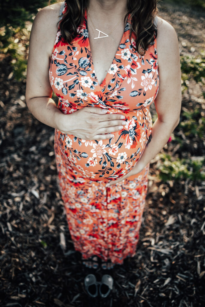 Overhead view of a pregnant belly in a floral coral dress, hands resting gently — beautiful inspiration for maternity photo outfit ideas.
