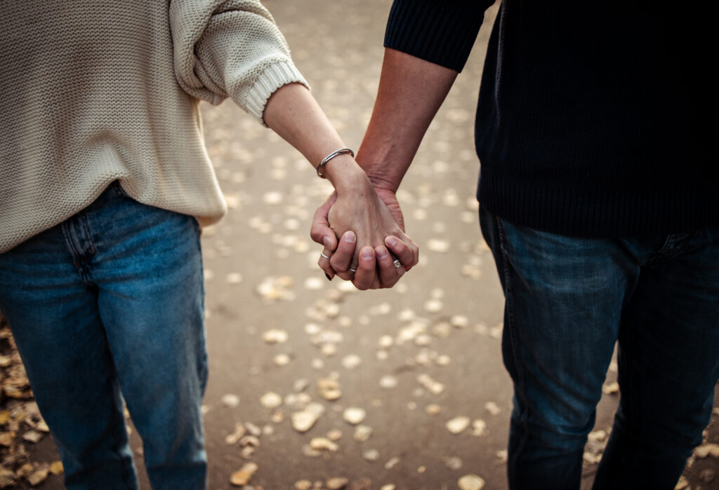 Love story photography: couple holding hands on a leaf-strewn path, navy and cream knits during an intimate autumn walk.