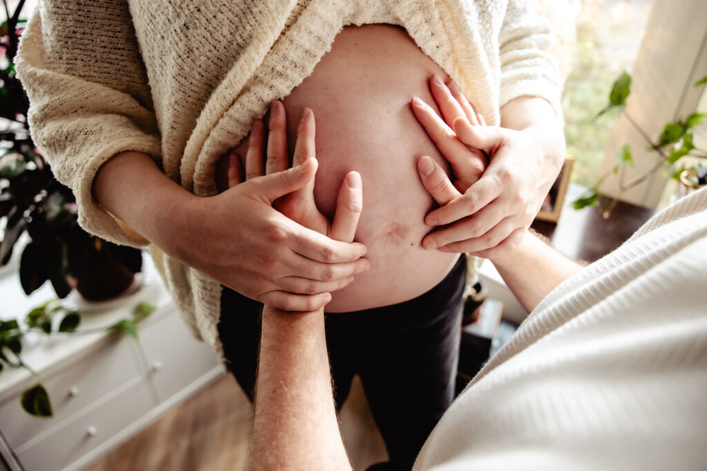 Close-up from an maternity photoshoot, highlighting the beauty of touch, connection, and the growing belly in soft window light.