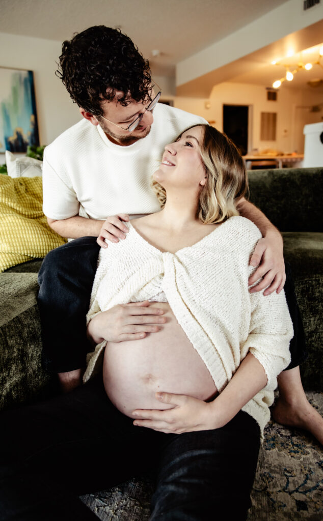 Candid at home maternity photo session in Edmonton showing a couple sharing laughter and love in their cozy living room.
