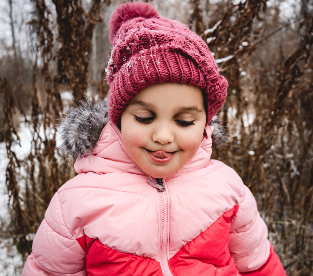 Child in a pink winter jacket and hat playing outside in the snow during outdoor Christmas photos Edmonton.