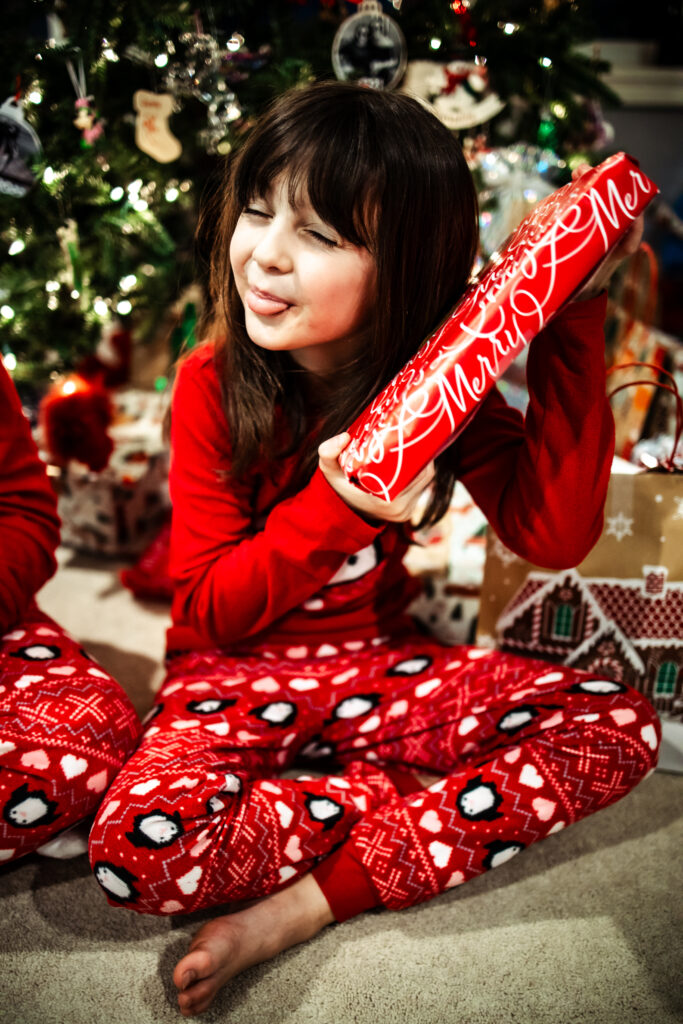 child in Christmas pajamas opening presents by the tree during cozy in home Christmas photos Edmonton session.