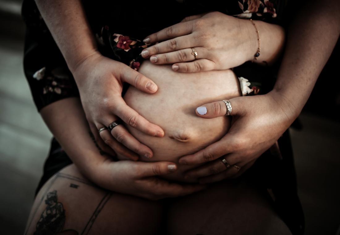 Hands supporting a pregnant belly during maternity session, symbolizing emotional and physical birth support in Edmonton.