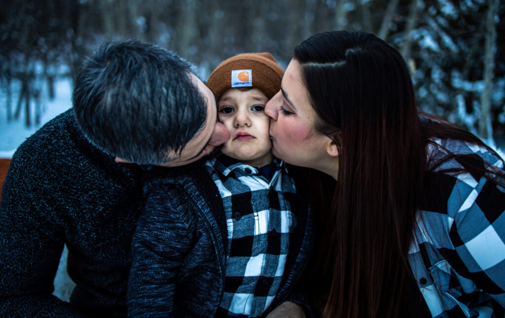 Parents kissing their child on both cheeks during a cozy winter family session at one of the intimate photoshoot locations Edmonton offers.