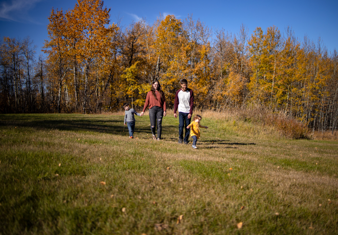 A family walking hand in hand through an open field surrounded by fall colours at one of the natural photoshoot locations Edmonton is known for.