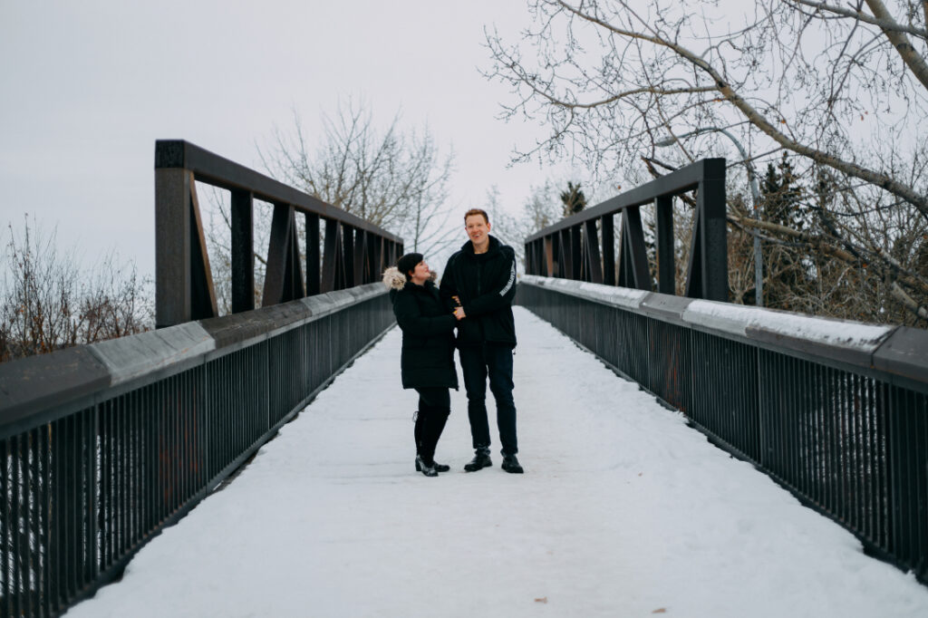 A couple walking together across a footbridge in winter.