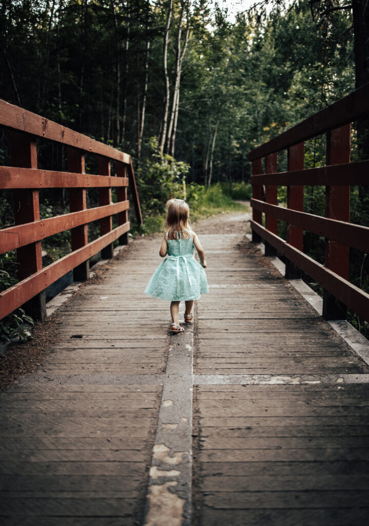 A toddler walking confidently across a wooden bridge, photographed during a family session at one of the storybook-style photoshoot locations Edmonton has.