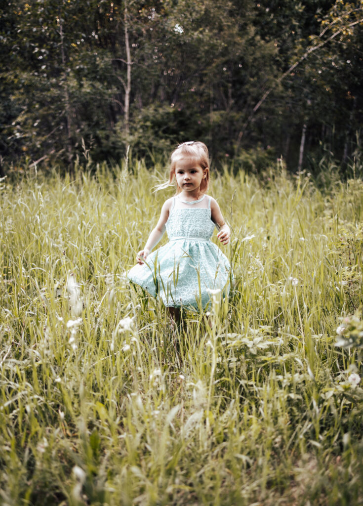A young child standing in tall grass surrounded by nature Edmontons Millcreek ravine.