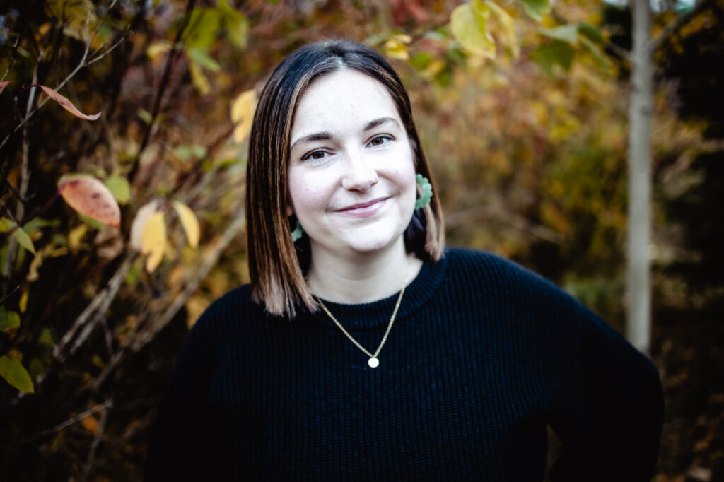 Portrait of a doula standing among autumn foliage, representing the caring services available through Edmonton doulas and midwives.