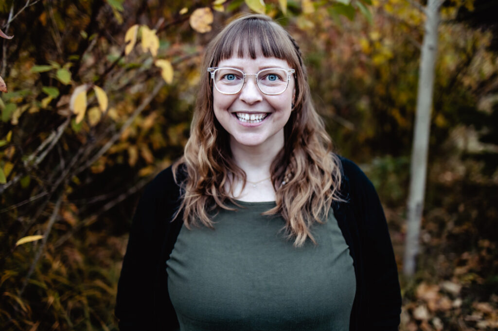 Smiling birth professional photographed outdoors in fall colours, offering pregnancy and postpartum support to local families.