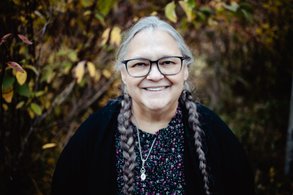Experienced birth professional with braided hair smiles during an outdoor portrait among autumn foliage.