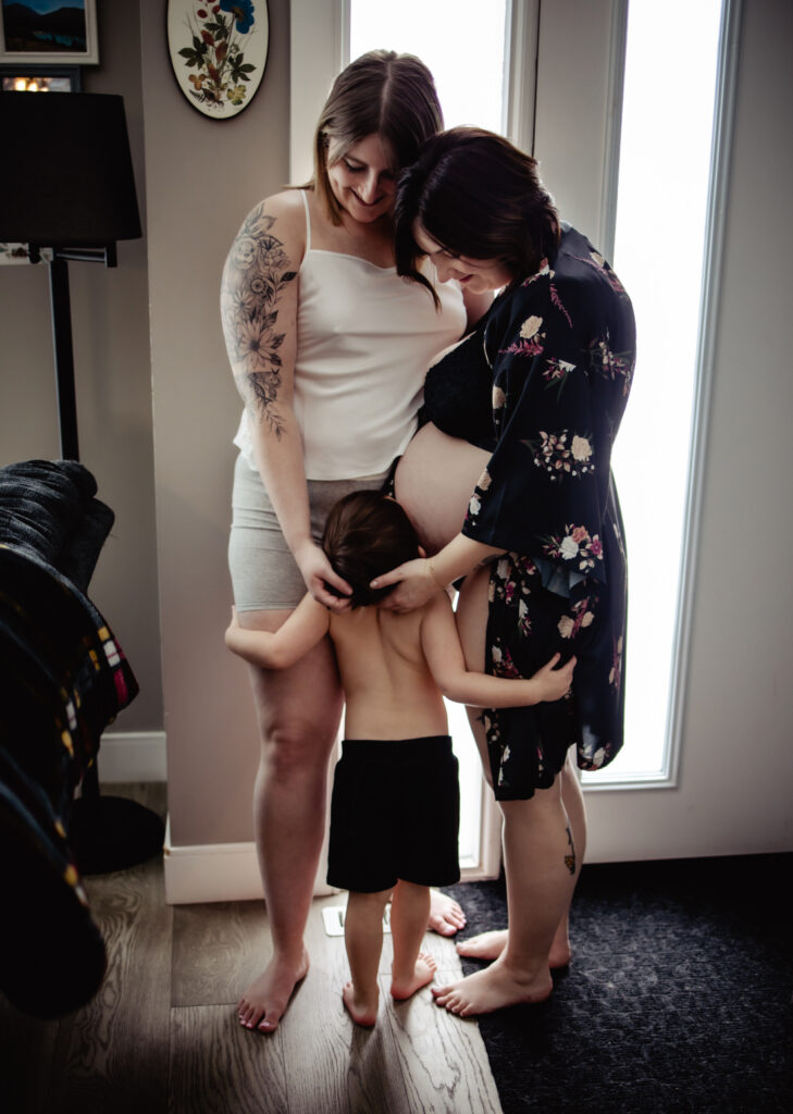 Pregnant couple and young child gather around a growing baby bump, celebrating family connection and pregnancy with support from Edmonton doulas and midwives.