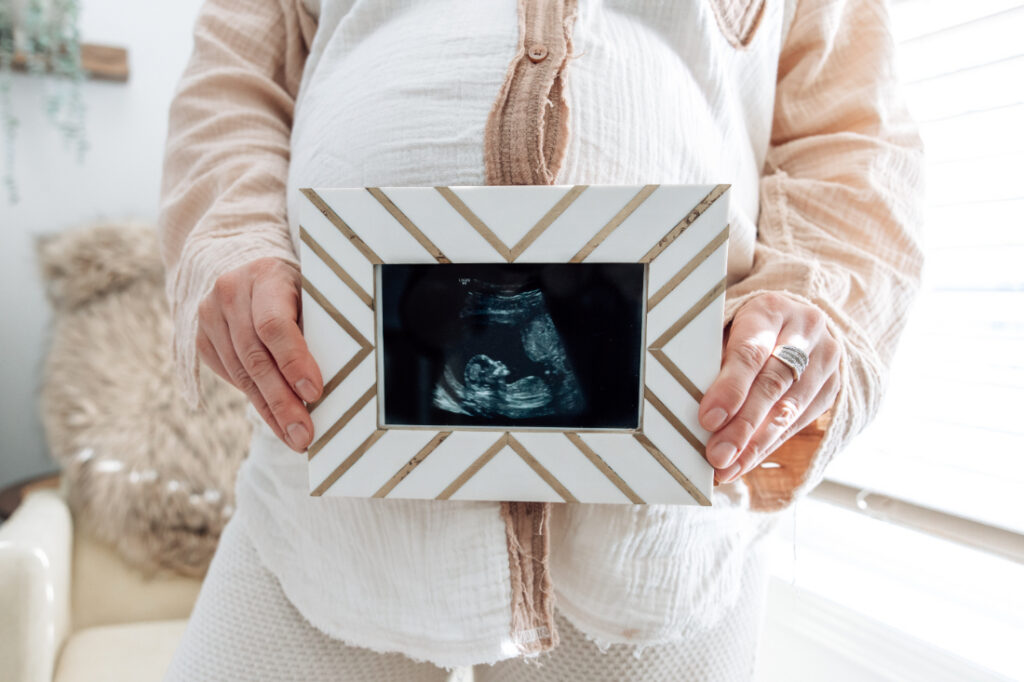 Pregnant mother holds a framed ultrasound photo during a bright lifestyle maternity session in her home.
