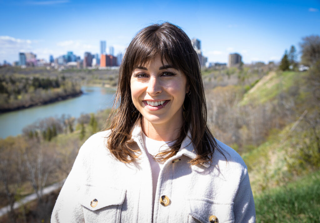 Portrait of a smiling birth support professional standing outdoors with the Edmonton skyline in the background.