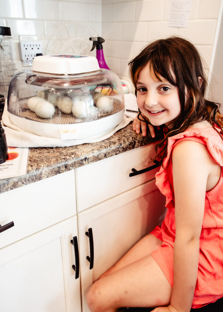 My daughter smiling beside our kitchen incubator, excited to check on the ten duck eggs that made it to lockdown.